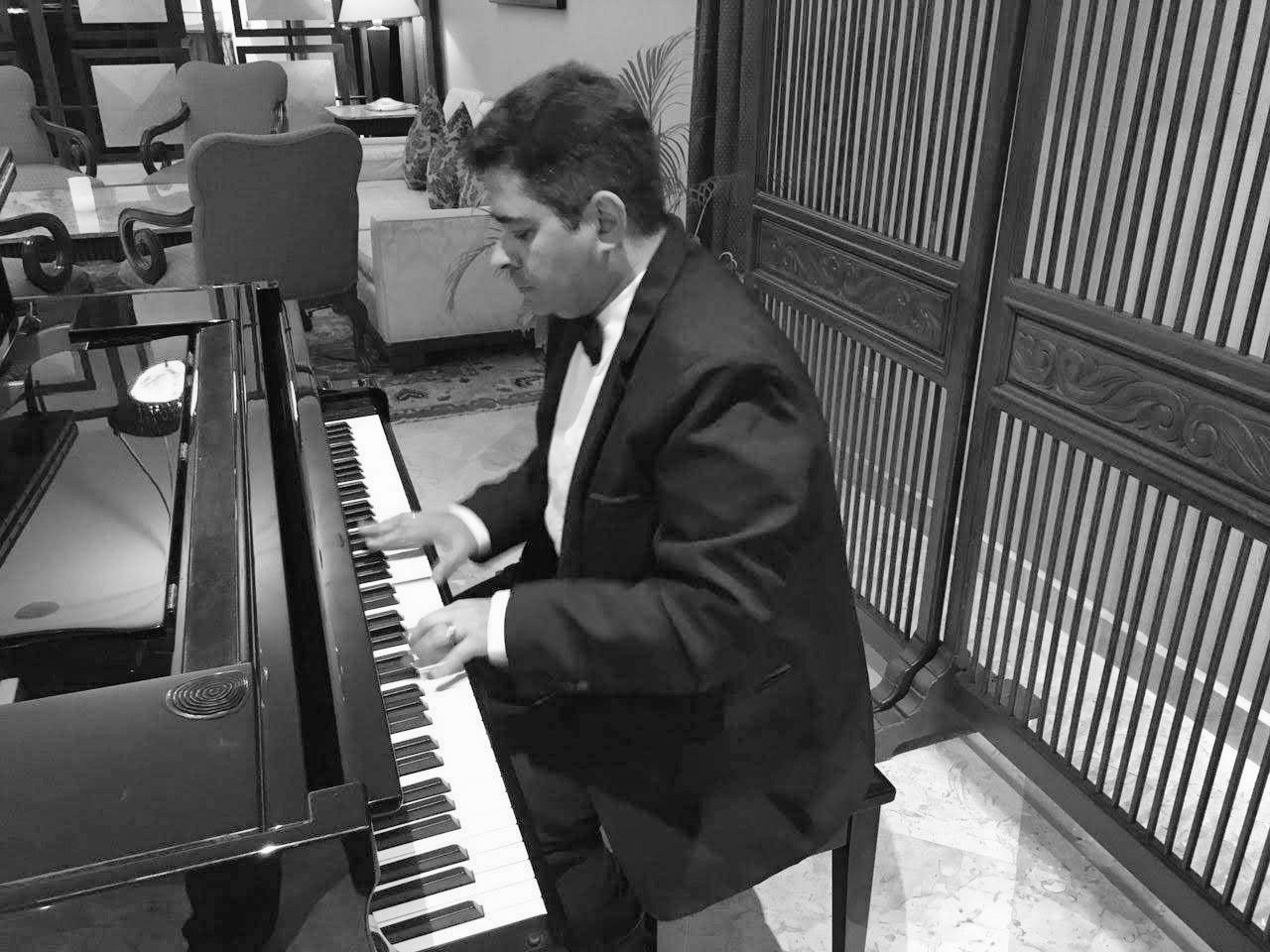 Yan Kayary de traje negro y moño, tocando un piano de cola junto a un biombo de madera