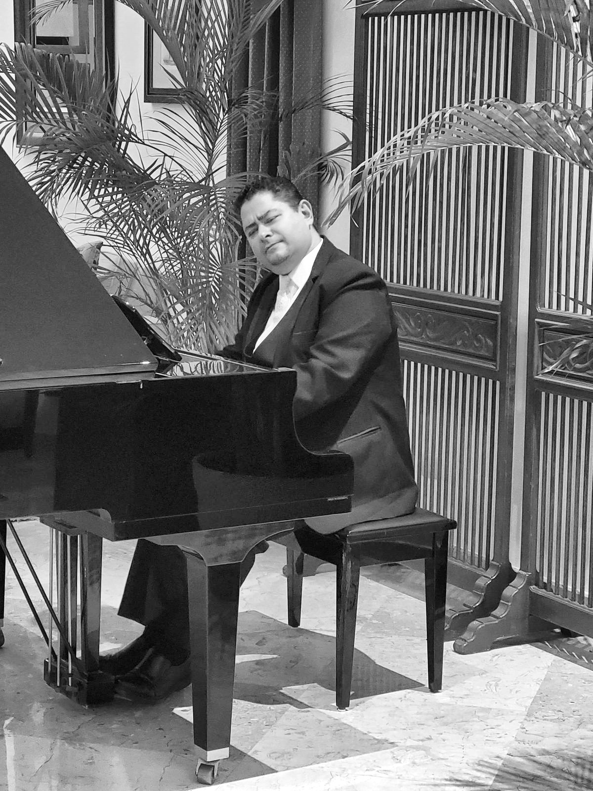 Yan Kayary al piano de cola, en blanco y negro, entre celosías