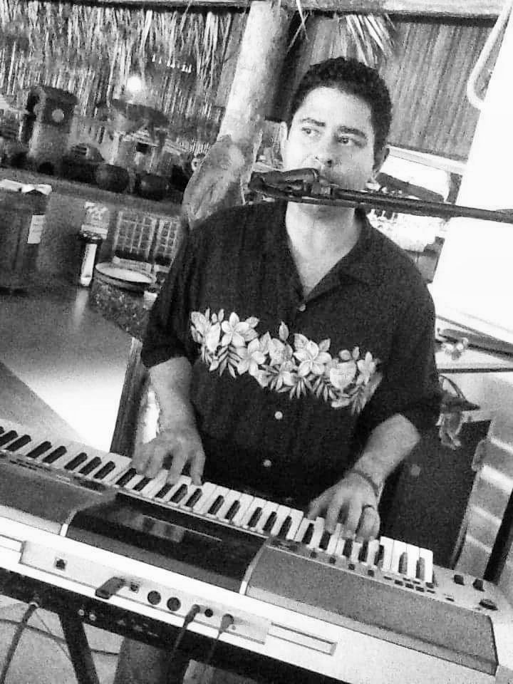 Yan Kayary al teclado y al micrófono, con camisa negra estampada