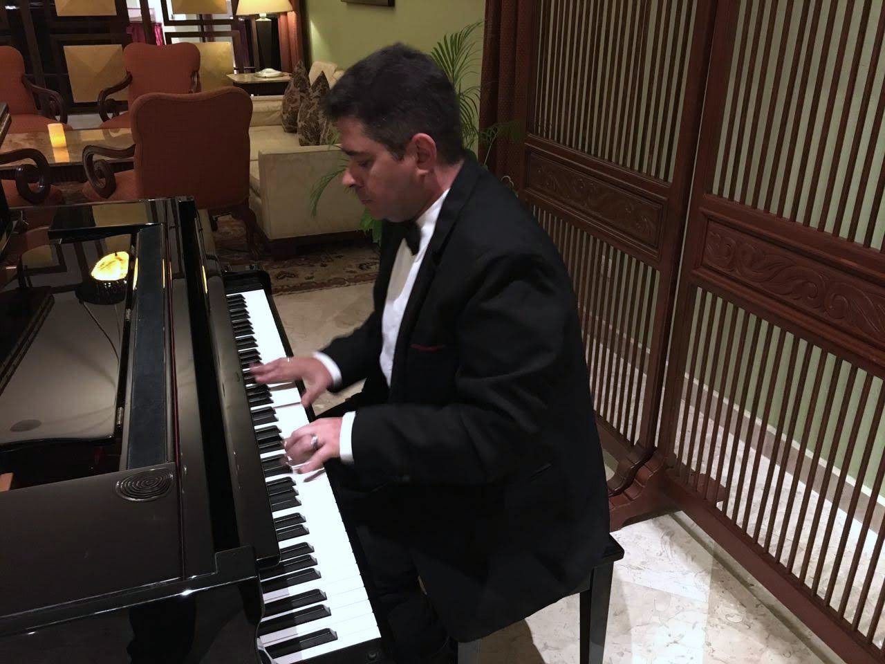 Yan Kayary de traje negro y moño, tocando un piano de cola junto a un biombo de madera