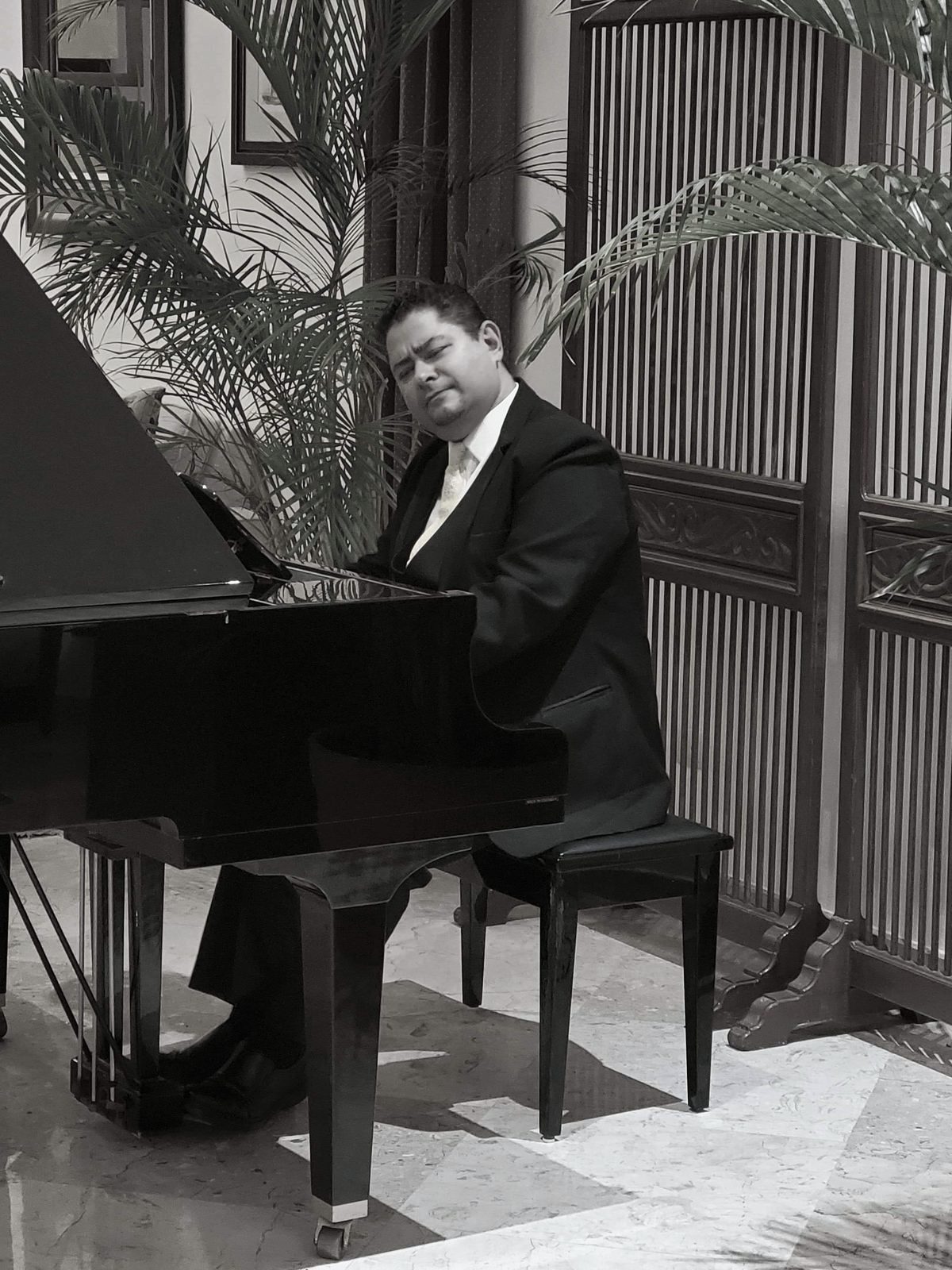 Yan Kayary al piano de cola, en blanco y negro, entre celosías