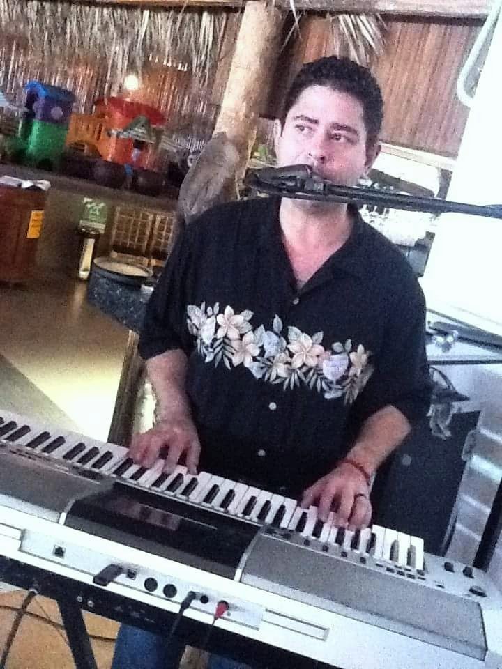 Yan Kayary al teclado y al micrófono, con camisa negra estampada