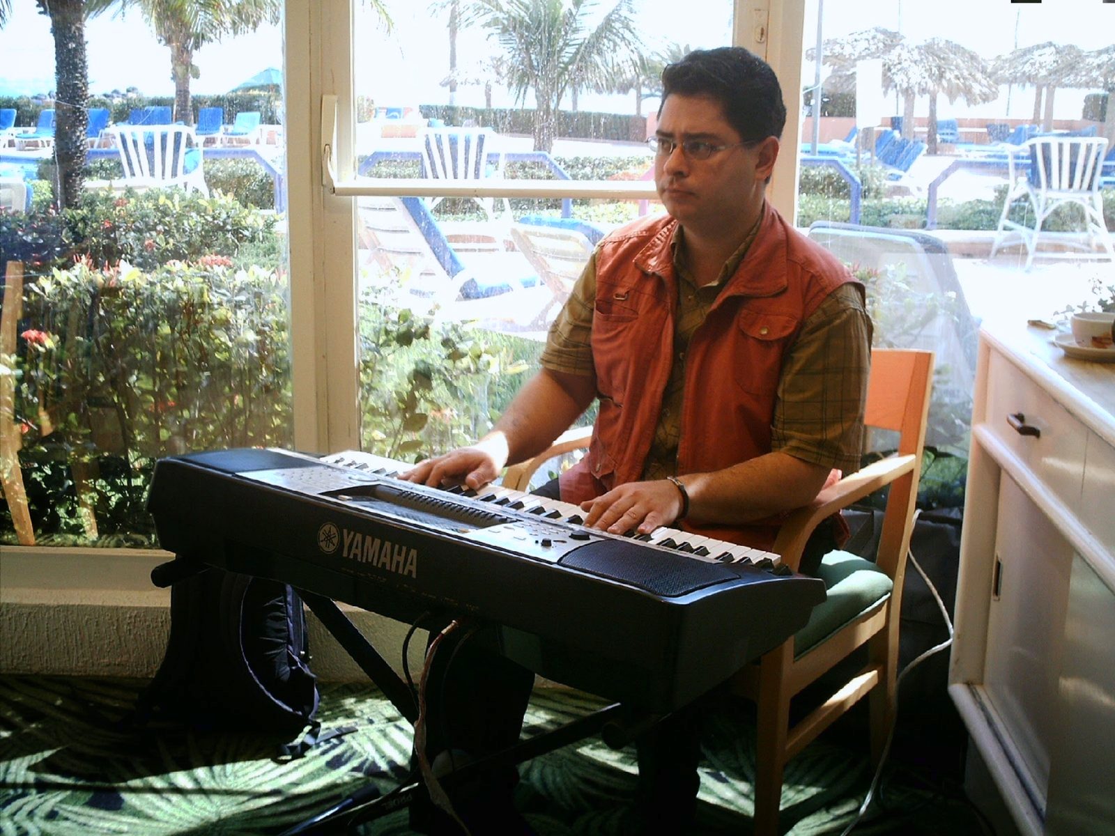 Yan Kayary con chaleco naranja, al teclado frente a grandes ventanas
